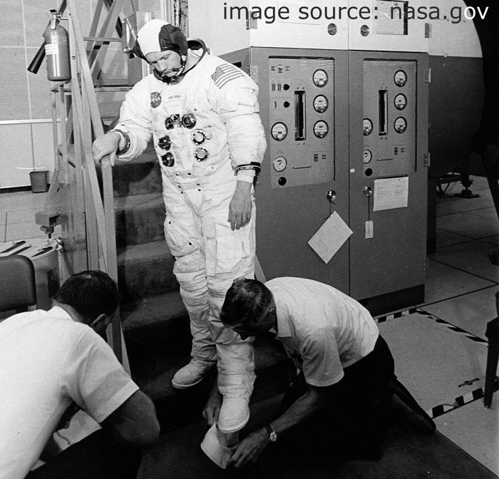 Ассистенты Nasa надевают на командира Neil Armstrong лунные ботинки